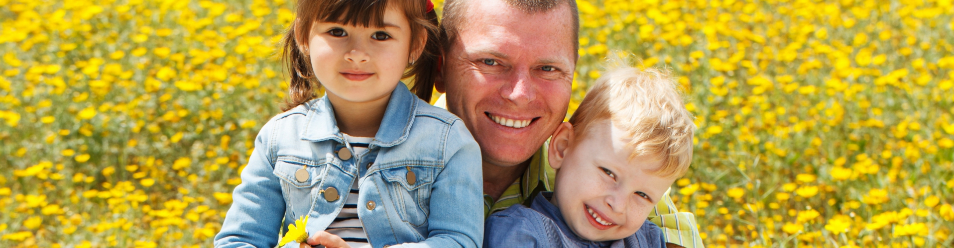 Father in wheelchair holding his two children in a daisy field